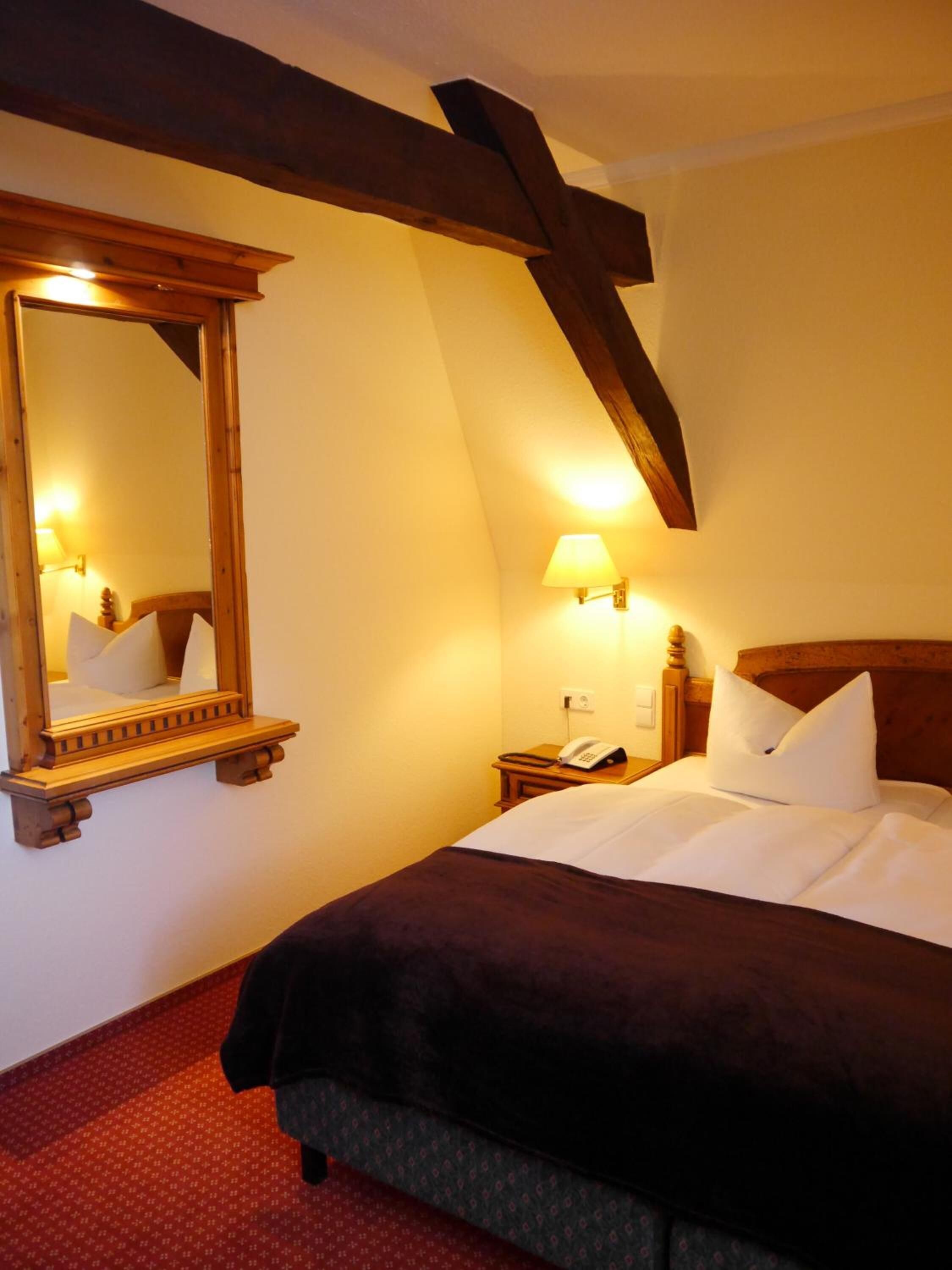 Una habitación de hotel con un espejo grande, una lámpara de noche, un teléfono y una cama bien hecha con almohadas.