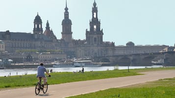 A cyclist on a paved path with a historic building and a river in the background.