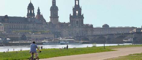 A cyclist on a paved path with a historic building and a river in the background.