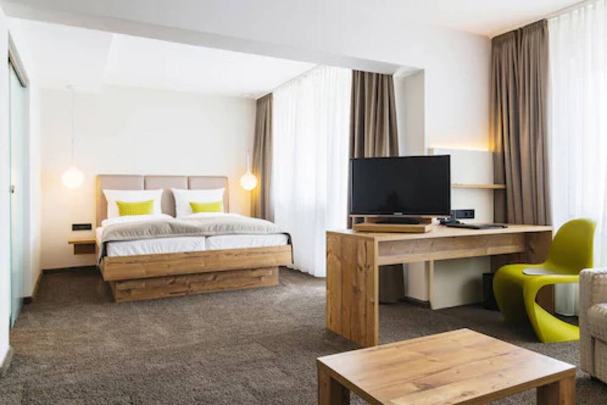 A hotel room with a bed, a desk with a TV, a chair, and a coffee table.
