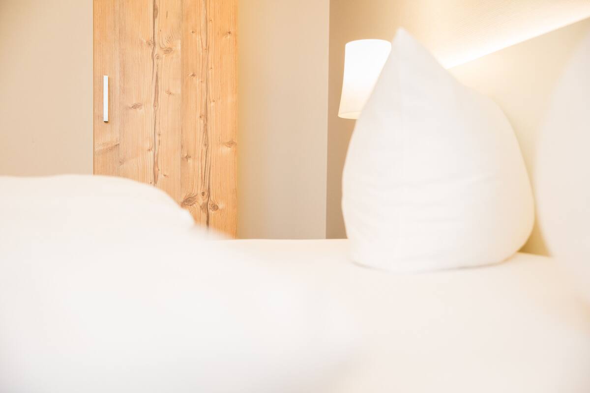 A hotel room with a wooden door, a white bed with a white pillow, and a bedside lamp.