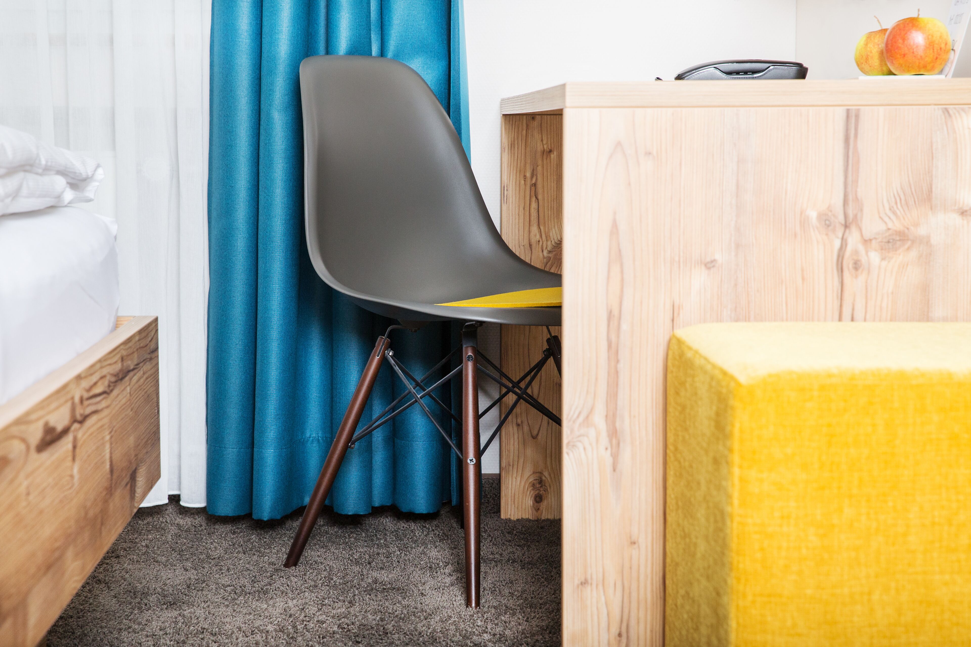 A room with a bed, a desk with a chair, a wooden table, and a yellow ottoman.