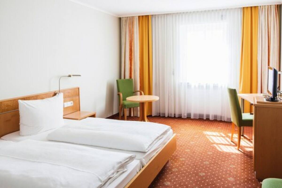 A hotel room with a bed, a desk, a chair, and a small table.