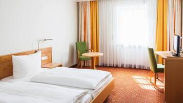 Quarto de hotel com cama, escrivaninha, cadeira e mesa pequena.
