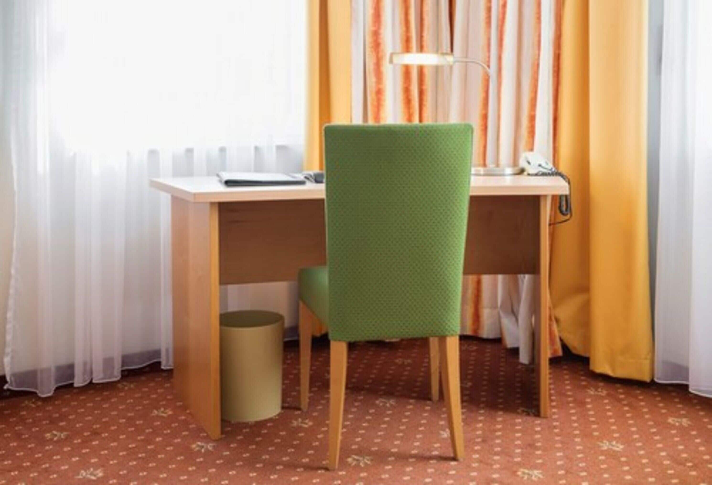 Ein Zimmer mit einem Holztisch, einem grünen Stuhl, einer Lampe und einem Mülleimer.
