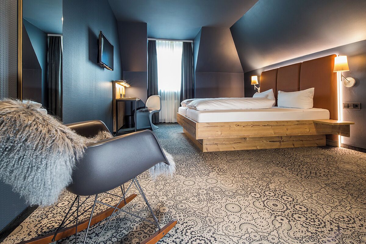 Een moderne hotelkamer met een groot bed, een houten hoofdeinde, een bureau met stoel en een televisie aan de muur.