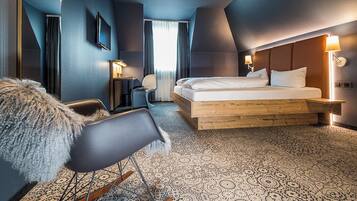 Een moderne hotelkamer met een groot bed, een houten hoofdeinde, een bureau met stoel en een televisie aan de muur.