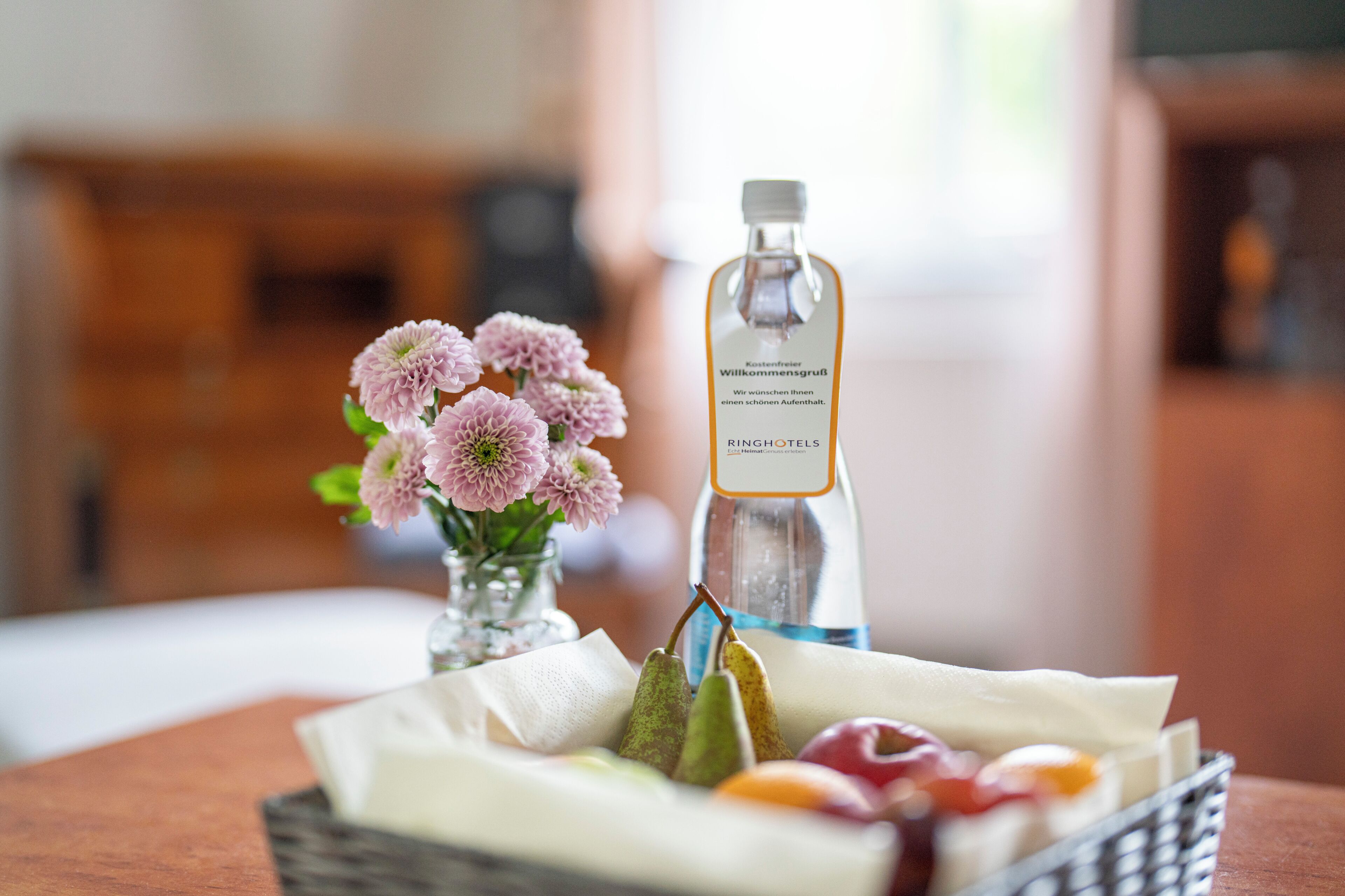 Eine Wasserflasche, ein Obstkorb und eine Vase mit Blumen auf einem Tisch.