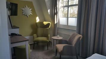 Habitación de hotel con escritorio, dos sillas, una mesita, un adorno con forma de sol y una ventana con cortinas.