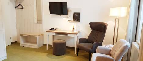 A hotel room with a desk, two chairs, a TV, a lamp, and a coat rack.