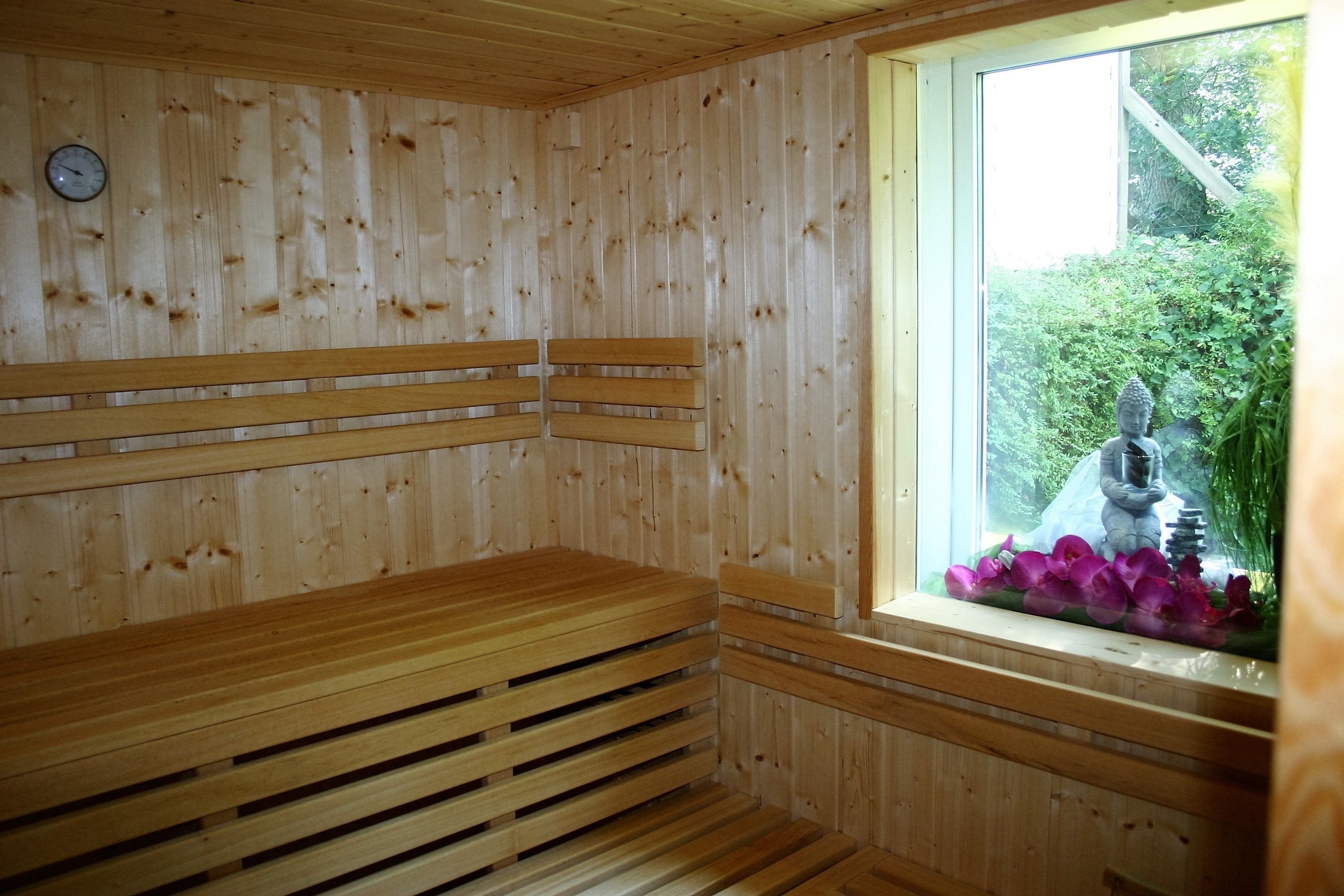 A wooden sauna with benches and a window with a statue and flowers.