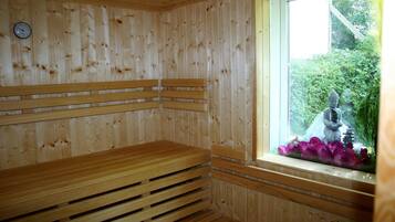 A wooden sauna with benches and a window with a statue and flowers.