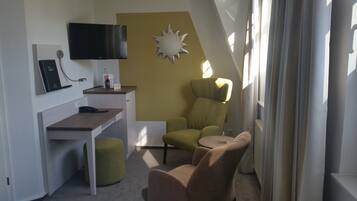 Ett kompakt hotellrum med ett skrivbord, en stol, en soffa, en tv och en solformad väggdekoration.