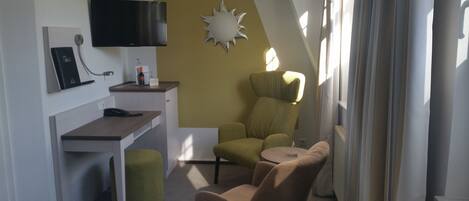 Habitación de hotel pequeña con escritorio, una silla, un sofá, televisor y un adorno de pared con forma de sol.