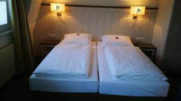 A room with two single beds, each with a nightstand and a wall-mounted lamp.