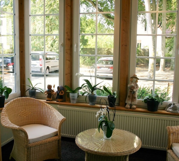 A room with large windows, wicker furniture, and potted plants.