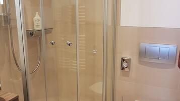 Un baño moderno con ducha de mampara de vidrio, inodoro blanco y un pequeño estante con artículos de aseo.