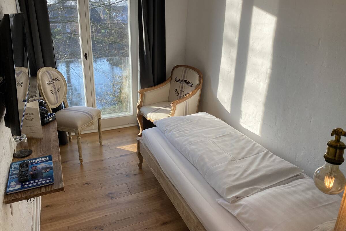Habitación con cama, una silla, una mesa con control remoto y vista a un cuerpo de agua a través de la ventana.