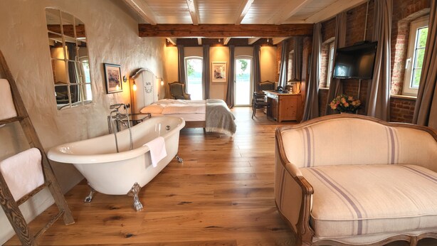 A room with a wooden floor, a bathtub, a sofa, a TV, and a window with curtains.