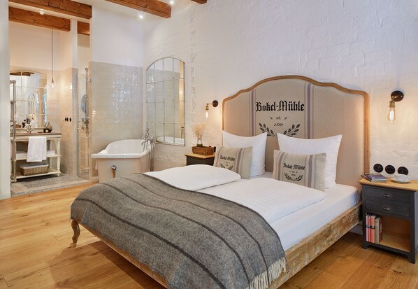 A spacious bedroom with a large bed, a wooden headboard, and a nightstand with books. - Bokel-Mühle am See (Bokel)