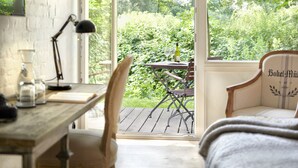A cozy room with a wooden desk, a chair, and a view of a lush garden through a large window.