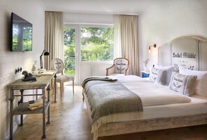 A bedroom with a large bed, a desk, and a chair. There is a window with curtains, a radiator, and a wall-mounted TV. - Bokel-Mühle am See (Bokel)