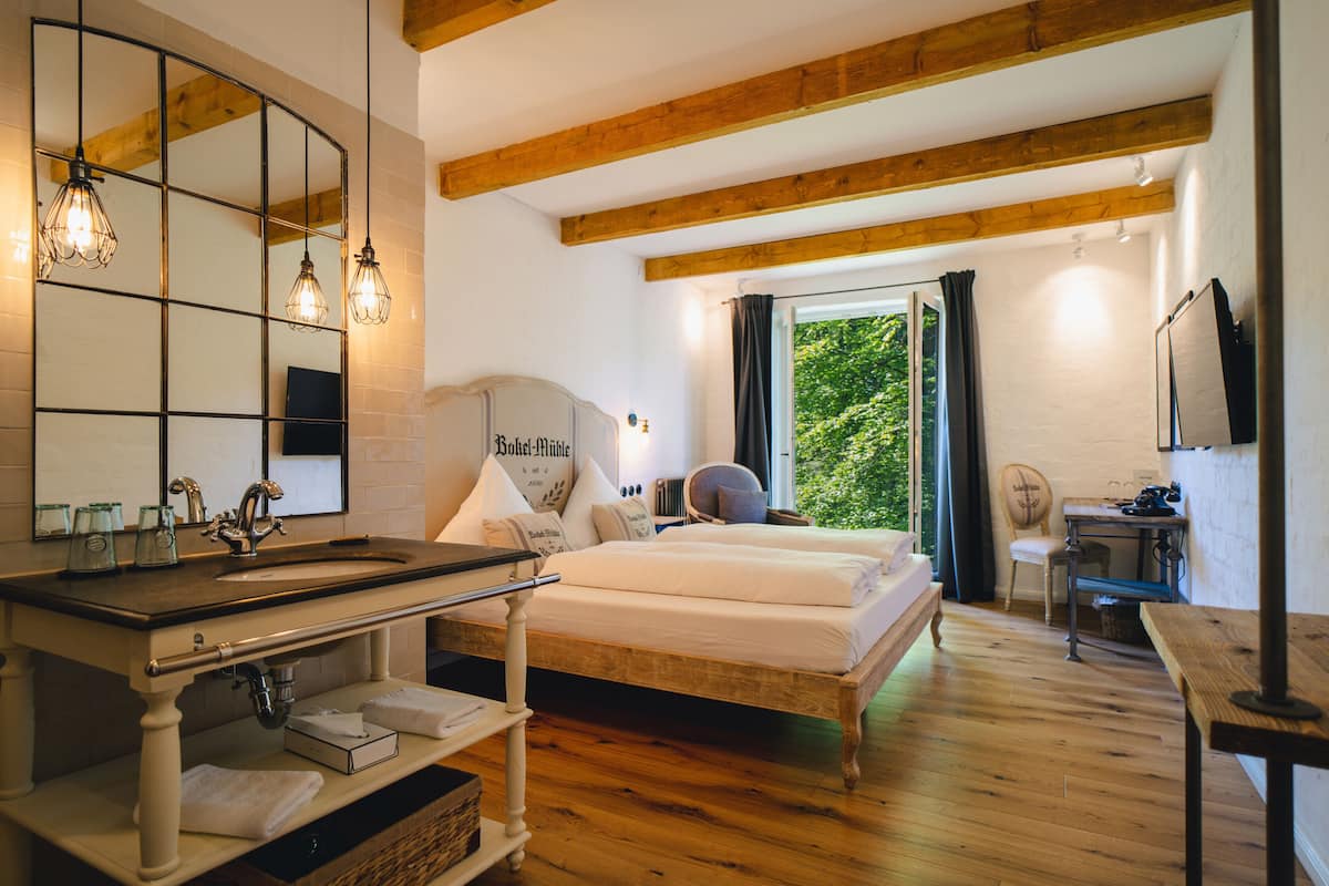 Un dormitorio con una cama de madera, un espejo grande, un escritorio de madera y una ventana con cortinas.