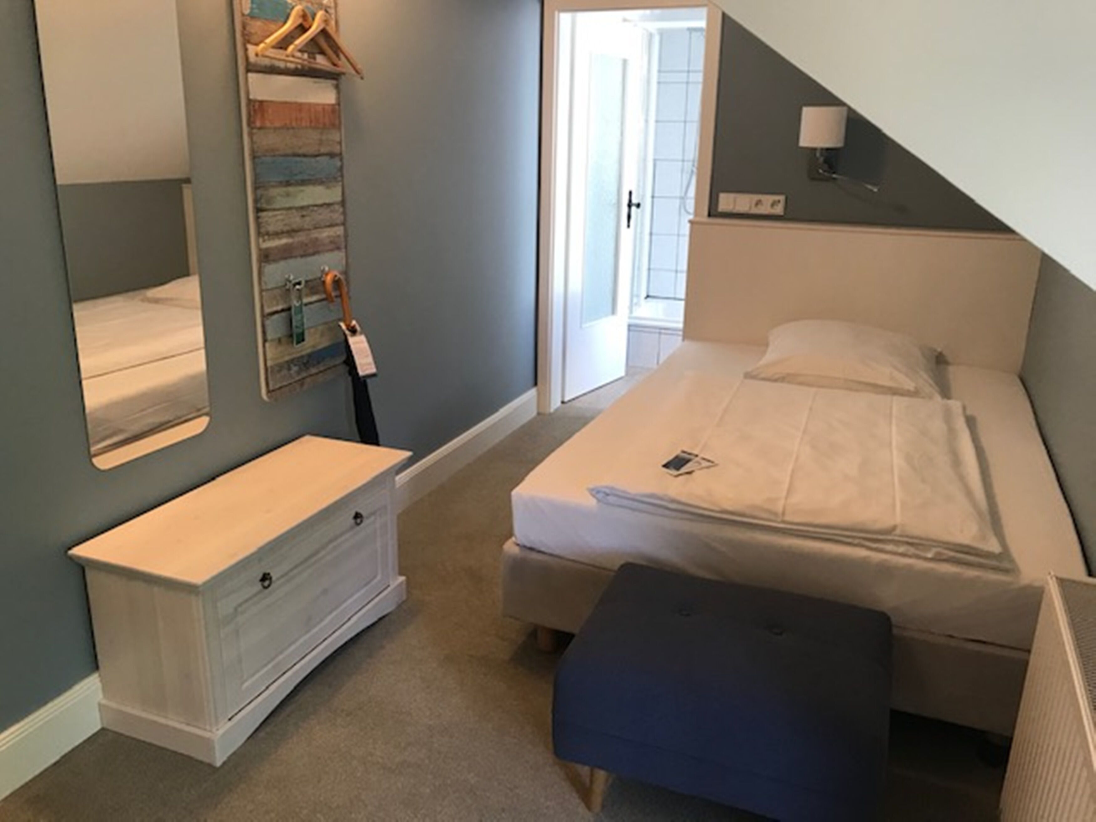 A bedroom with a bed, a dresser, a bench, a mirror, and a door leading to another room.