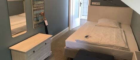 A bedroom with a bed, a dresser, a bench, a mirror, and a door leading to another room.