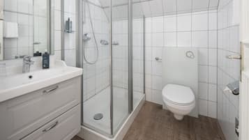 Un baño moderno con ducha envuelta en vidrio, un lavamanos blanco con espejo y un inodoro.