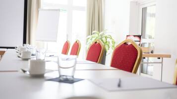 Ein Konferenzraum mit langem Tisch, roten Polsterstühlen, einer Whiteboard und einem Blumentopf.