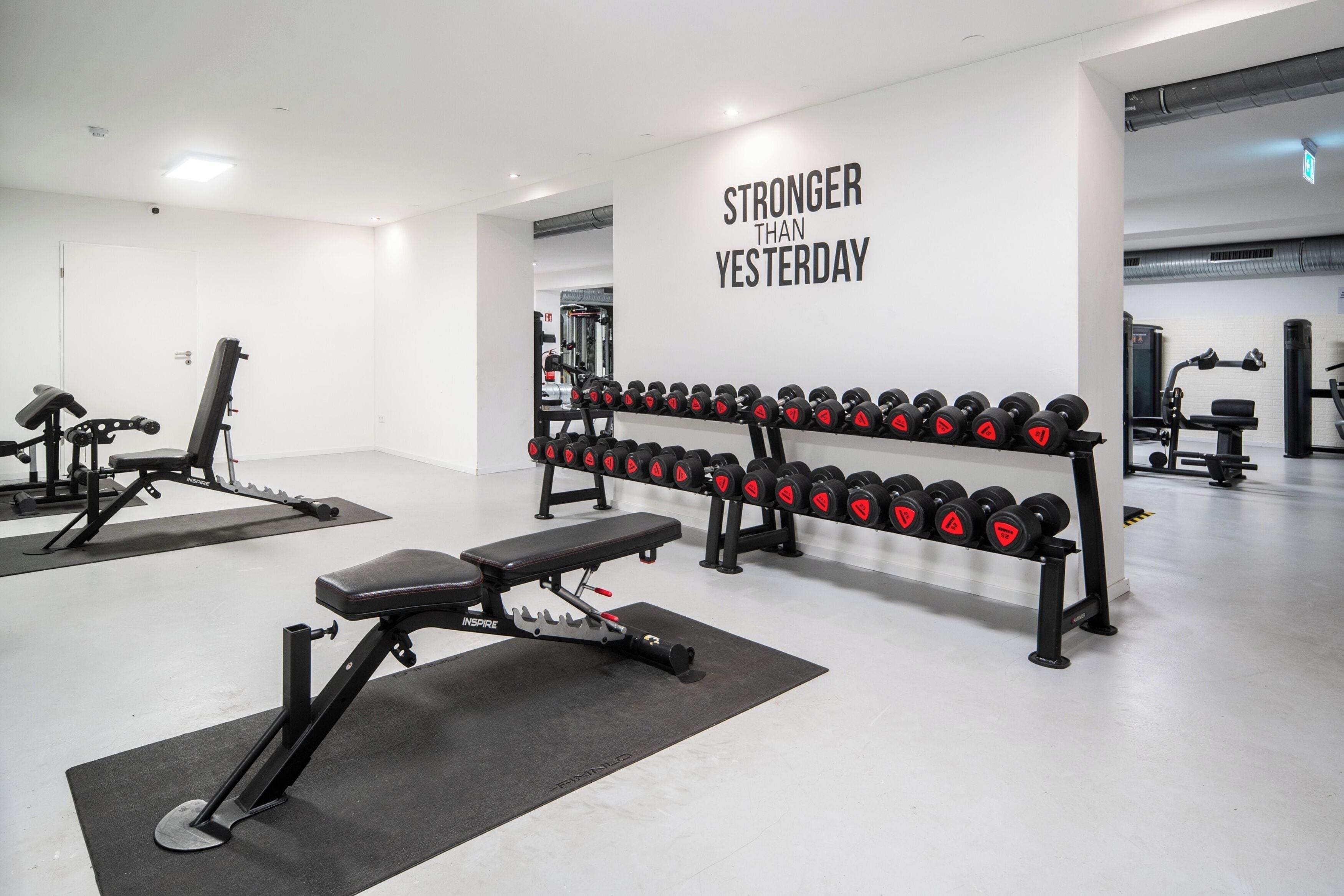 Un gimnasio con equipo de levantamiento de pesas, una banca y una frase motivacional en la pared.