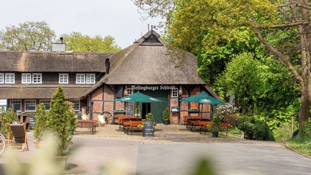 A traditional building with a thatched roof, outdoor seating, and a sign reading "Mellingburger Schluze".