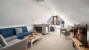 A modern loft-style room with a blue sofa, grey armchair, wooden coffee table, and a television.