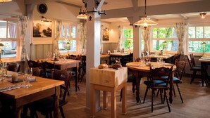 A dining area with wooden tables and chairs, ceiling fans, and natural light from windows.