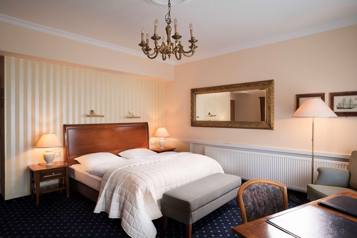 Une chambre d’hôtel comprenant un lit, des tables de chevet, une chaise, un bureau et un lustre.
