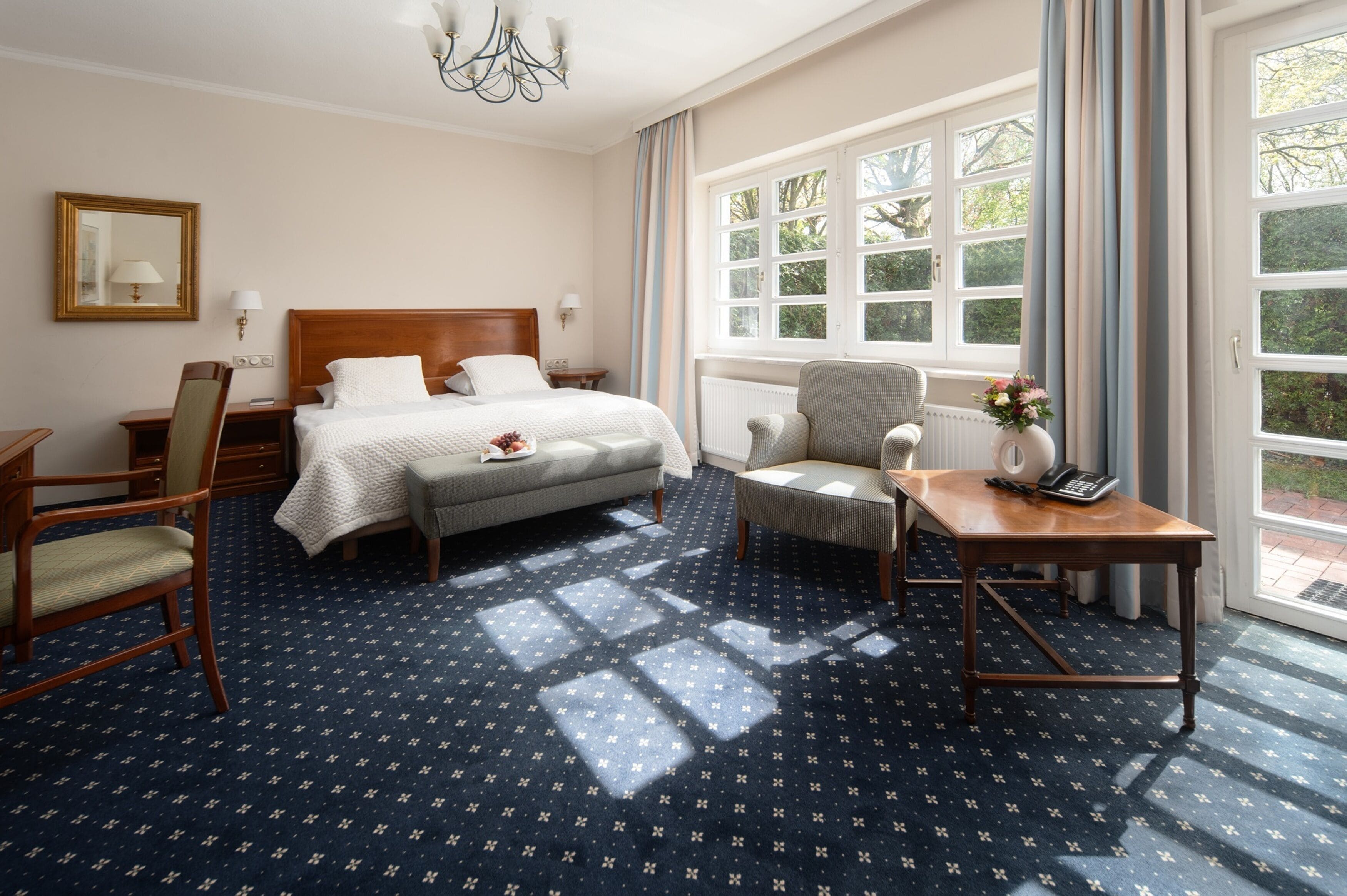 A hotel room with a bed, a desk, a chair, a small table, and a window with curtains.