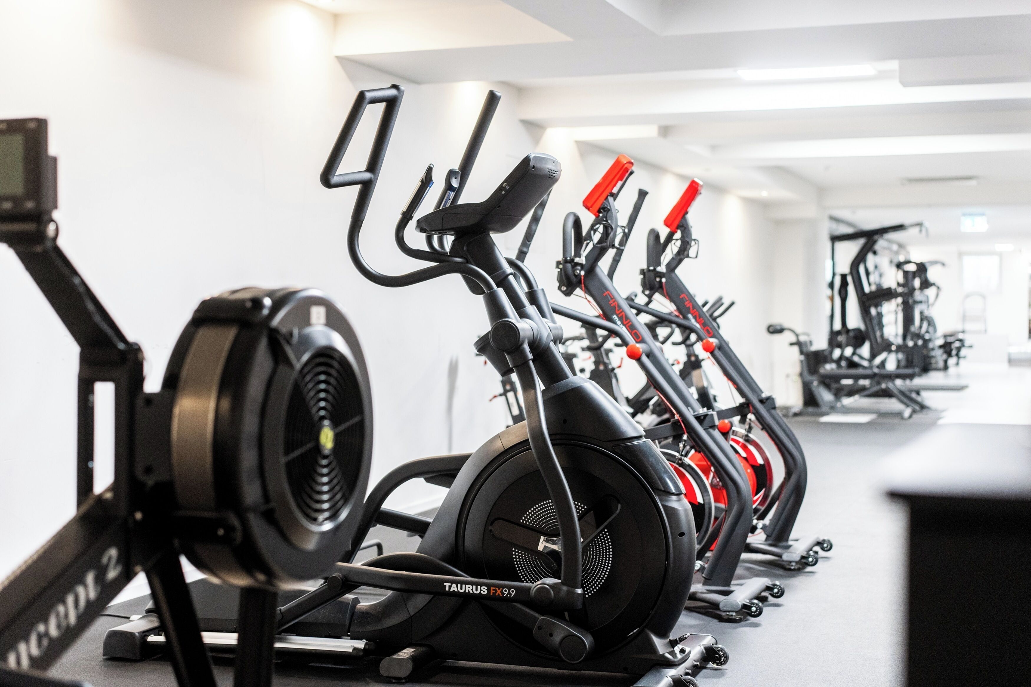 Une rangée de vélos d’appartement dans une salle de sport, avec un plafond et des murs blancs.