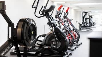 Une rangée de vélos d’appartement dans une salle de sport, avec un plafond et des murs blancs.