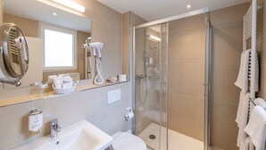 Un baño moderno con ducha de vidrio, lavamanos blanco y un espejo grande.