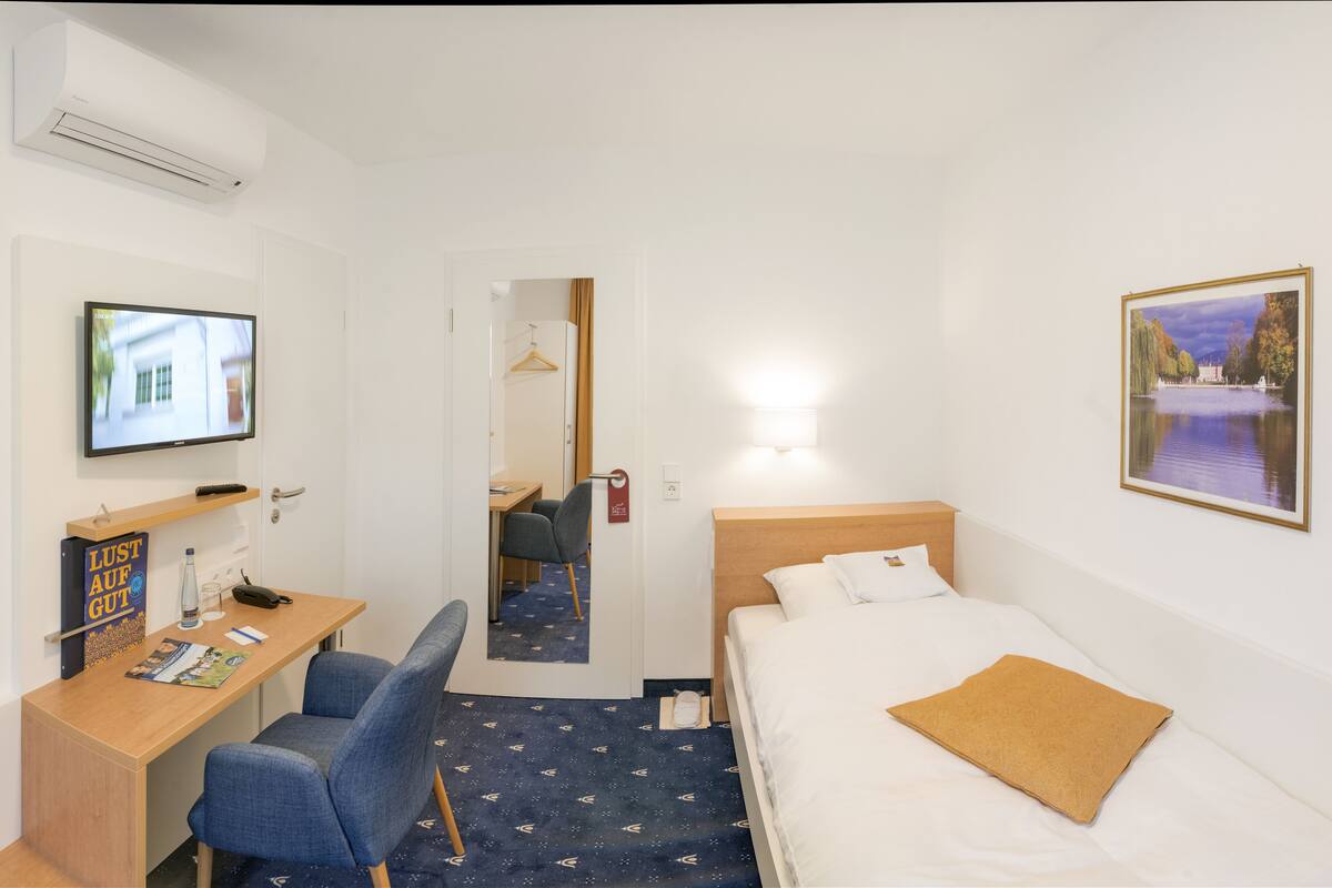 A hotel room with a bed, desk, chair, TV, and a painting on the wall.