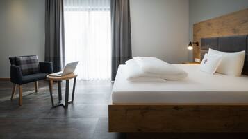 Una habitación de hotel moderna con una cama, un escritorio con una computadora portátil, una silla y una mesita de noche con una lámpara.