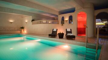 Ein Swimmingpool mit Liegestühlen und einem rot beleuchteten Bogen.