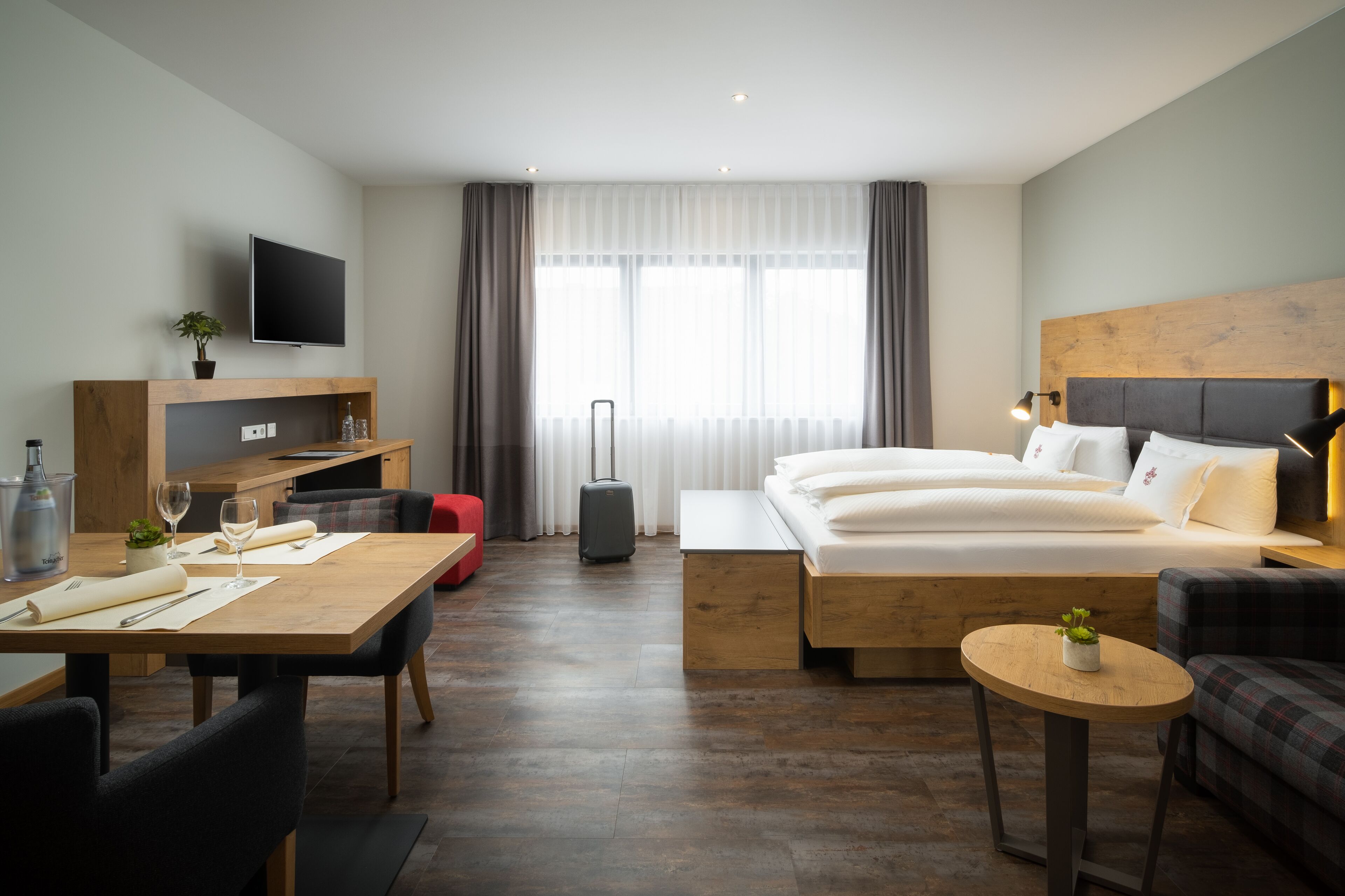 Una habitación de hotel moderna con una cama de madera, un escritorio con silla, una mesita redonda pequeña y un sofá.
