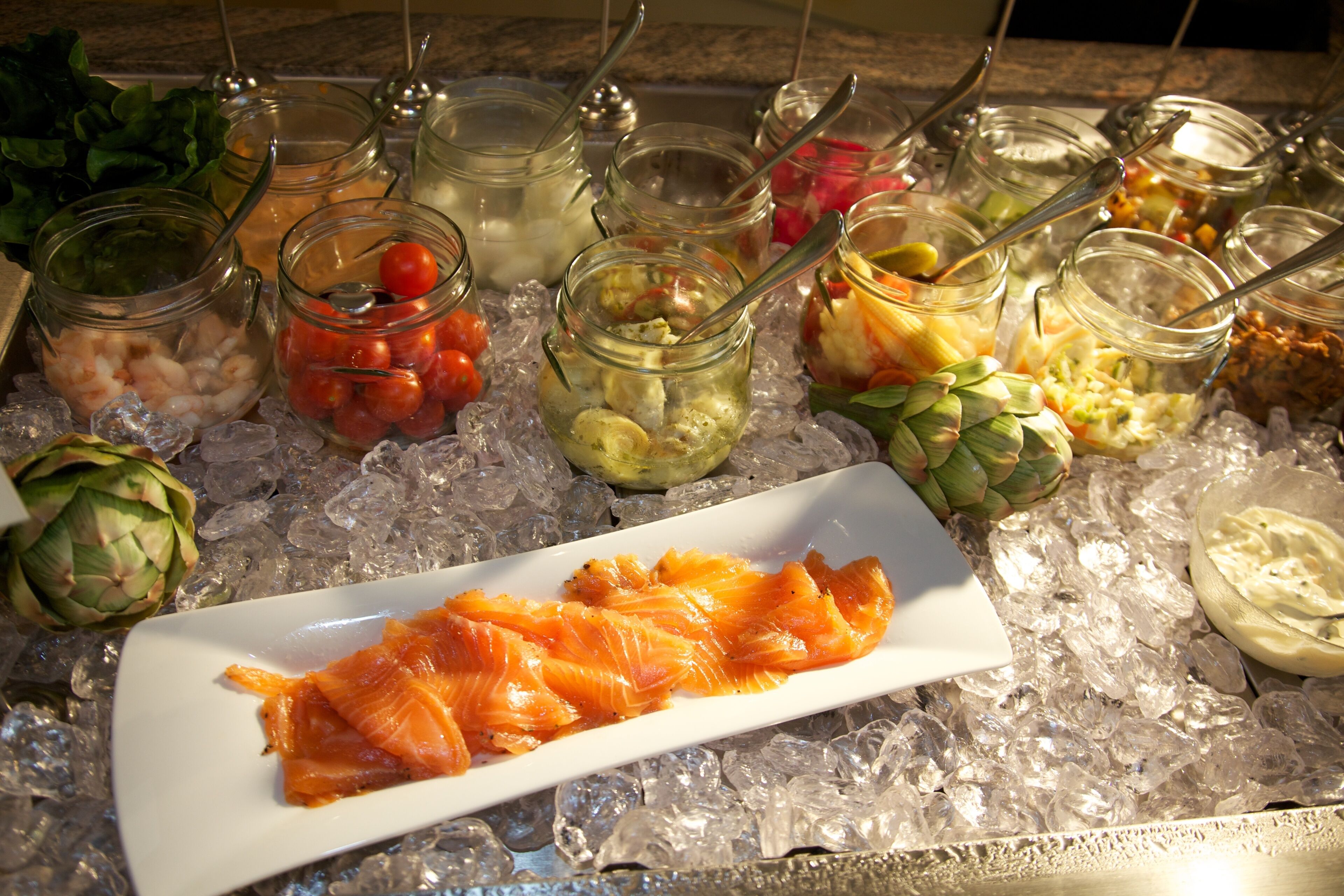 Een buffet met diverse etenswaren op ijs, waaronder zalm, groenten en dipsauzen.