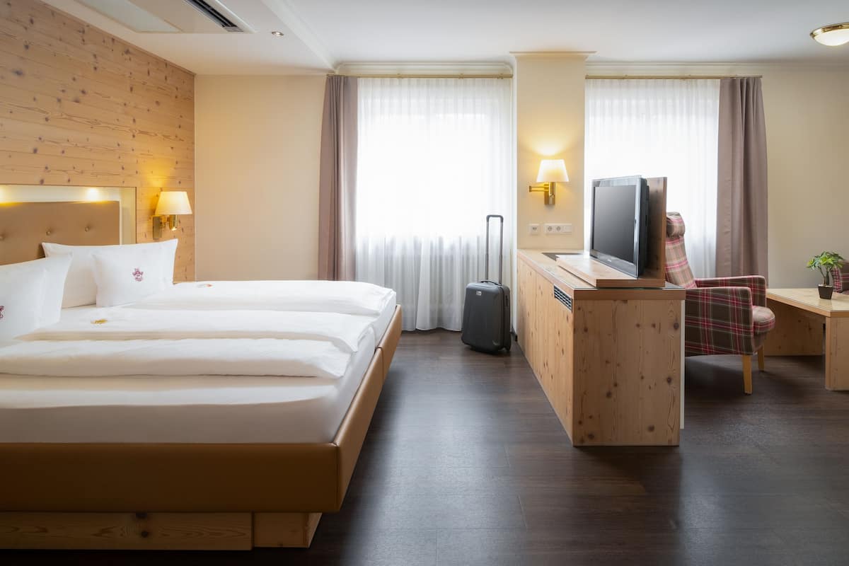 Habitación de hotel con una cama grande, un escritorio con televisor, una silla y una pequeña mesa con una planta.