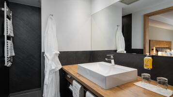 A modern bathroom with a large white sink, dark marble walls, and a wooden vanity.
