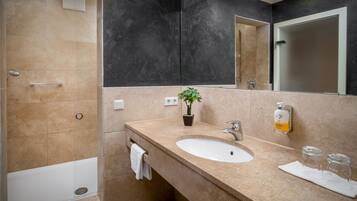 A modern bathroom with a beige sink, a mirror, a potted plant, and a shower.