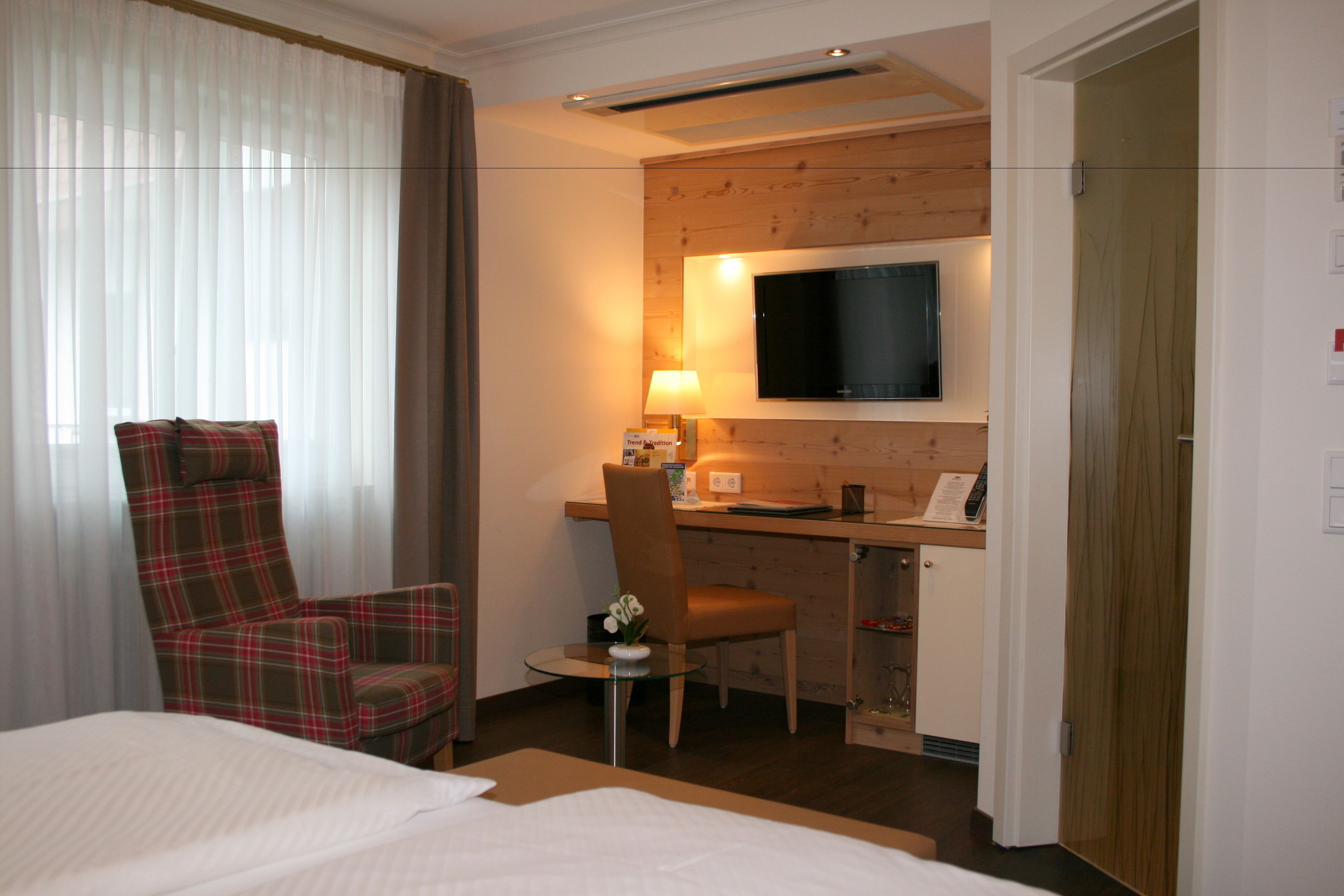 Une chambre d’hôtel comprenant un lit, un bureau avec une chaise, une télévision et une petite table avec une lampe.