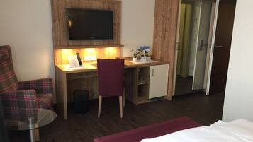 A hotel room with a wooden desk, a television, a chair, a small cabinet, and a bed.